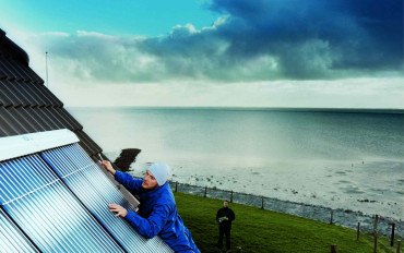 Man installing Solar Thermal panels at the roof of house/building with a sea view on the coast